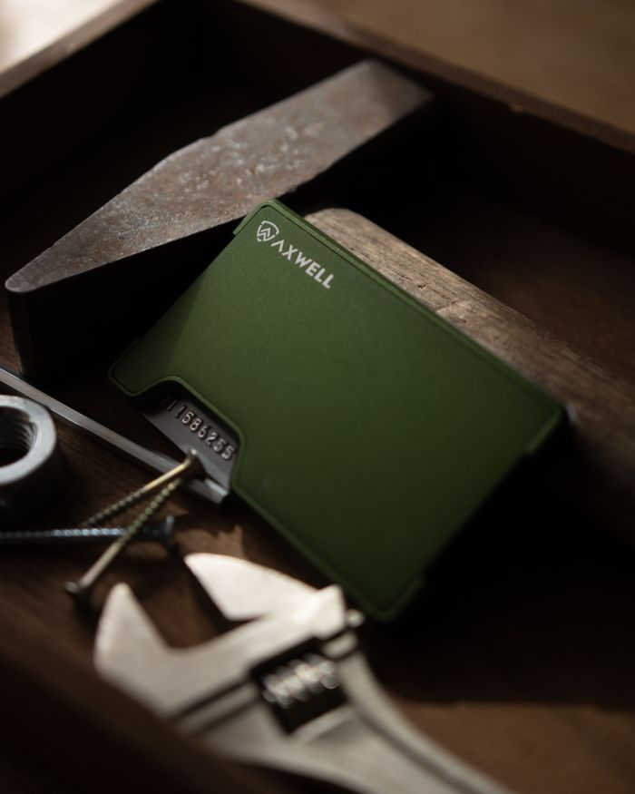A green metal wallet placed with tools in a wooden tray, captured in a moody, artistic style.